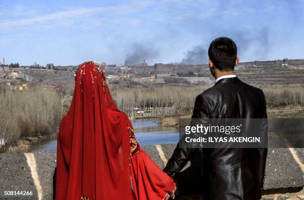 Couple hold hands for a wedding photo as they look at smokes rising over the district of Sur in Diyarbakir on February 3, 2016 after clashes between...