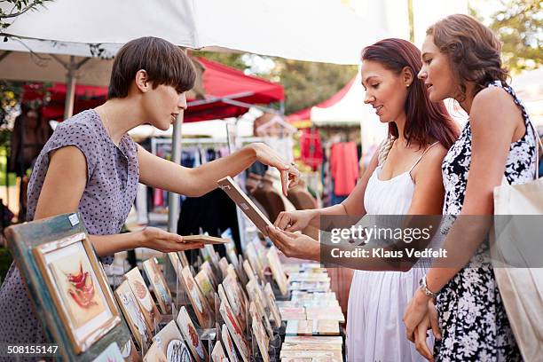 girlfriends looking at small paintings at market - art and craft show stock pictures, royalty-free photos & images