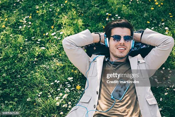 young man relaxing in the park - young man listening to music on smart phone outdoors stockfoto's en -beelden