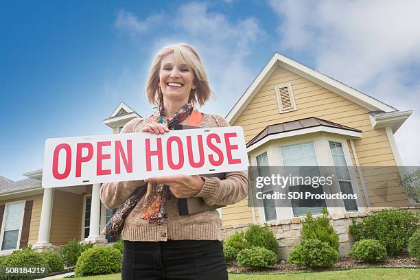 mature real estate agent holding open house"" sign in front yard - estate agent sign stockfoto's en -beelden