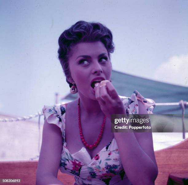Italian actress Sophia Loren wearing a floral patterned dress pictured eating an orange segment on a yacht in 1965.