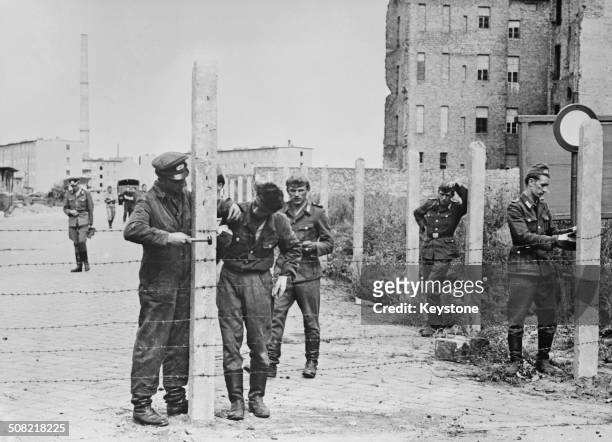 Soldiers of the East German National People's Army erecting barbed wire fences to close off a street in preparation for the construction of the...