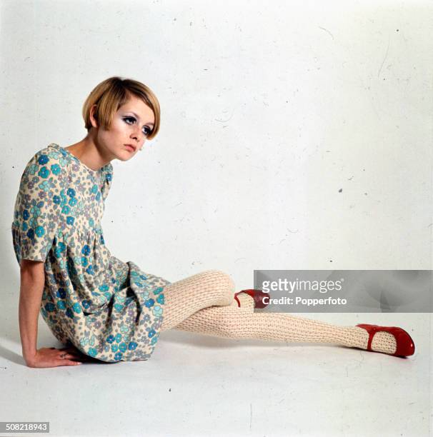 Sixties Fashion - English fashion model Twiggy posed wearing a short floral baby-doll style dress with white knitted tights and red shoes circa 1966.
