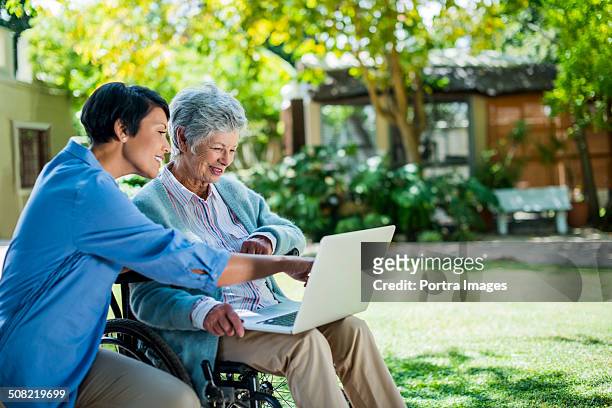 caretaker and disabled senior woman using laptop - retirement community stock pictures, royalty-free photos & images