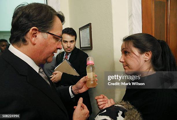 Flint resident Jessica Owens shows Sen. Gary Peters , a baby bottle full of contaminated water, during a news conference after attending a House...