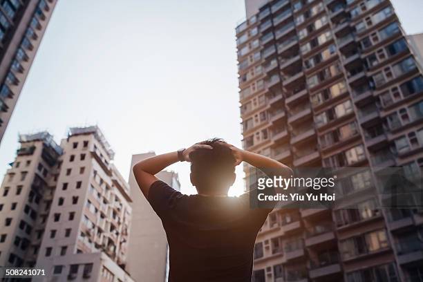 distraught man holding his head in front of city - hoffnungslosigkeit stock-fotos und bilder