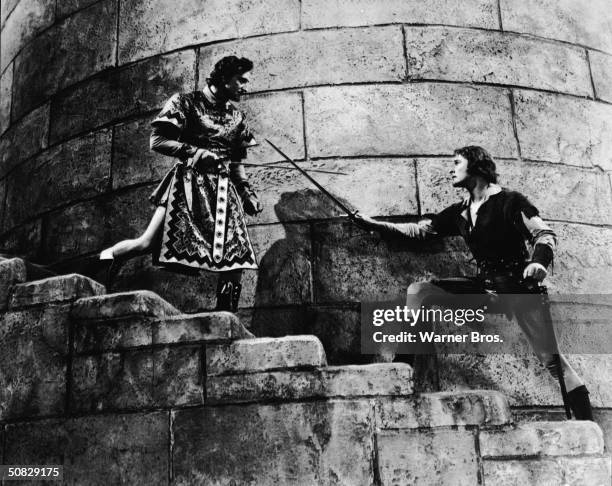 Actors Errol Flynn and Basil Rathbone duel on a castle stairwell in a still from the film, 'The Adventures of Robin Hood,' directed by Michael Curtiz...