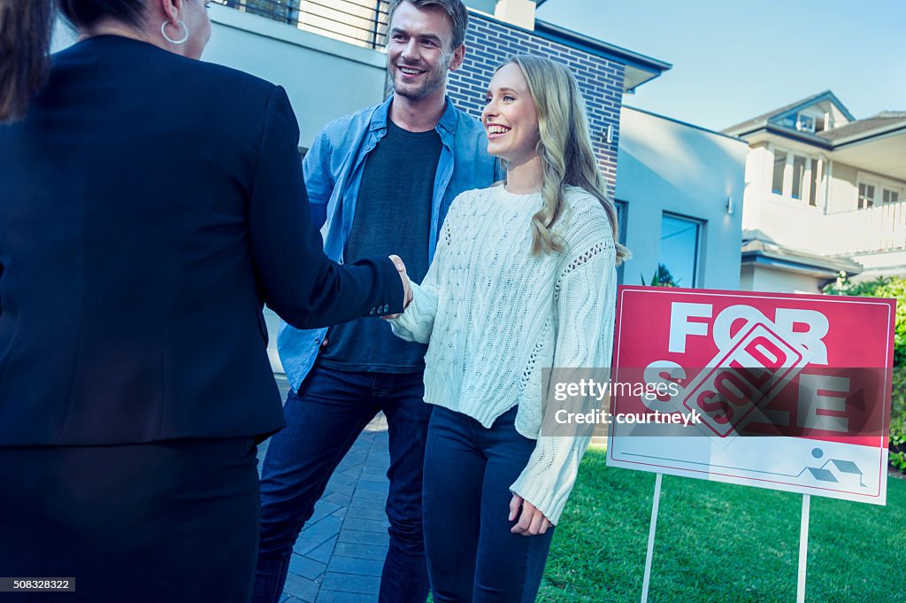 Couple standing in front of a new home with agent.