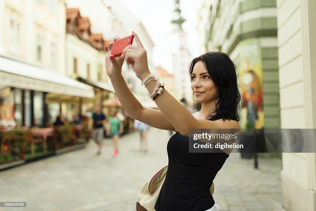 Hermosa Chica sonriente y tomando autofoto en la calle