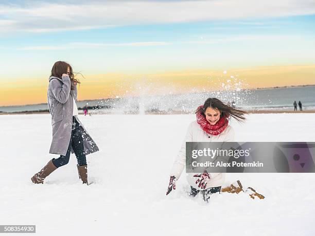 two sisters, teenager girls, play snowballs at the brighton beach - enterntainment stock pictures, royalty-free photos & images