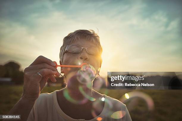 senior woman blowing bubbles - bubble wand photos et images de collection