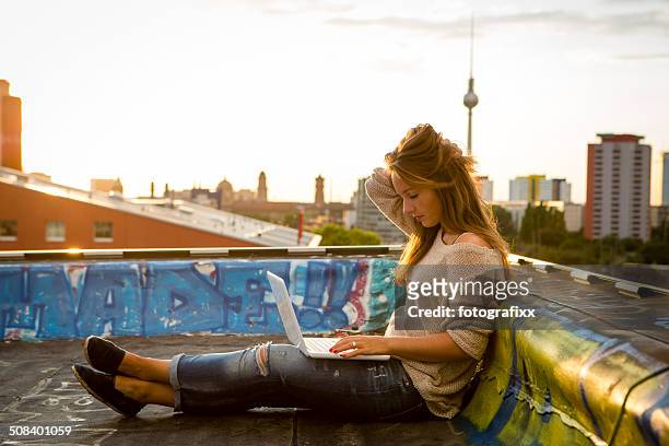 junge frau sitzt auf dem dach, arbeitet auf laptop-gegenlicht - berlin fernsehturm stock-fotos und bilder