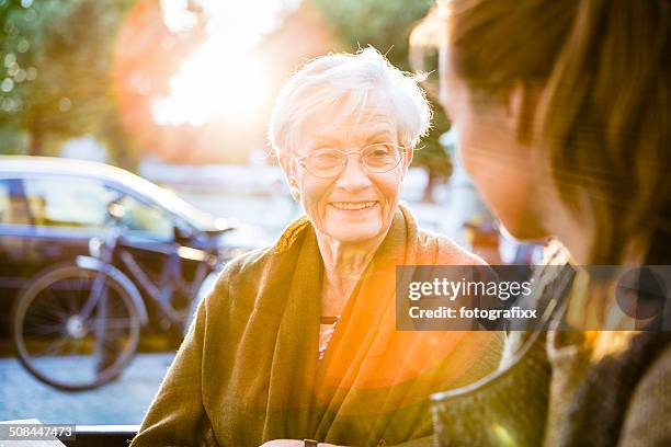 young and senior woman sit together in a sidewalk cafe