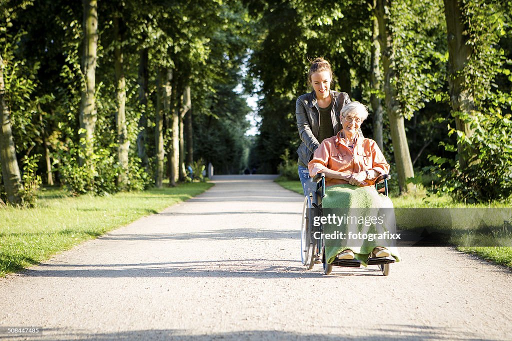 Young woman pushing senior lady in wheelchair through a park