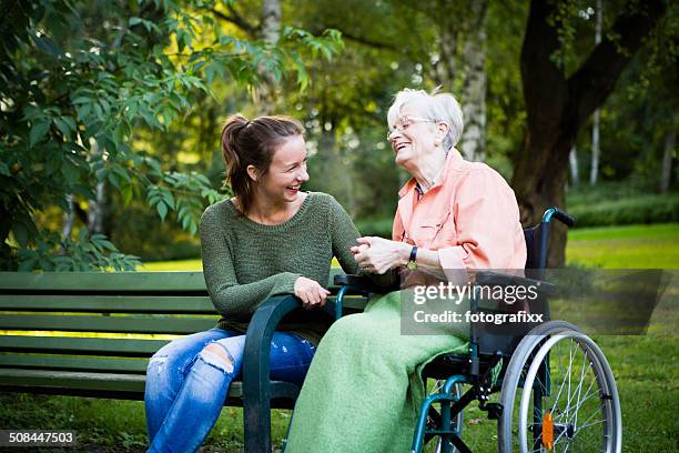 senior woman in wheel chair laughs with young woman - communities public park stock pictures, royalty-free photos & images