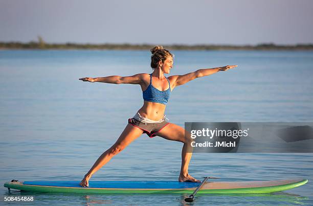 yoga on a stand up paddle board - practioners enjoy serenity of paddleboard yoga stockfoto's en -beelden