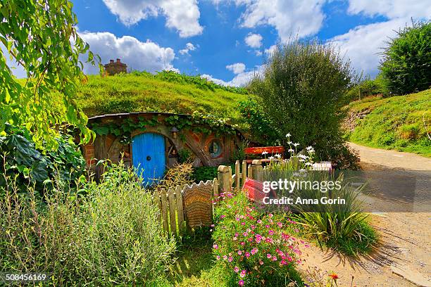 Small hobbit-hole with blue door and picket fence at Hobbiton film set in Matamata, New Zealand, on partly cloudy summer afternoon.