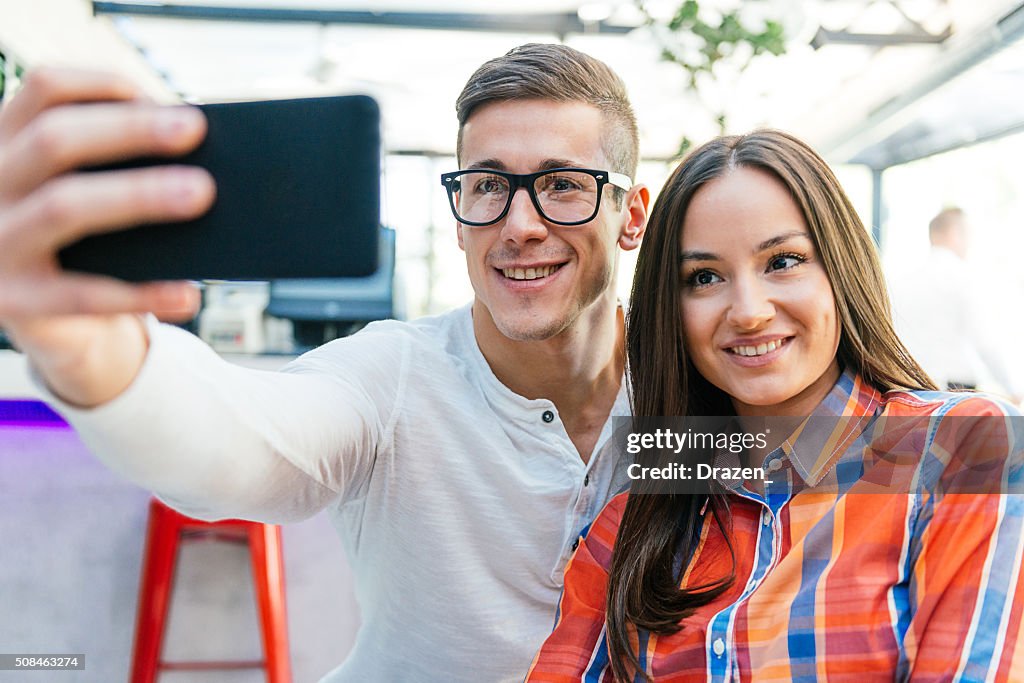 Cheerful young couple making selfie in modern interior and smiling