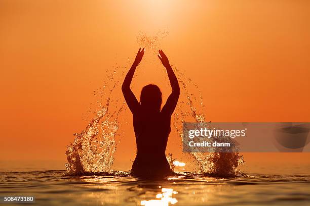 beauty model girl splashing water with her hands. teen girl swimming and splashing on summer beach over sunset. beautiful woman in water - bathing in sunset stockfoto's en -beelden