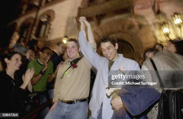 Gay couple clasp hands in response to applause from a large crowd as they emerge from City Hall after applying for a marriage license in the early...