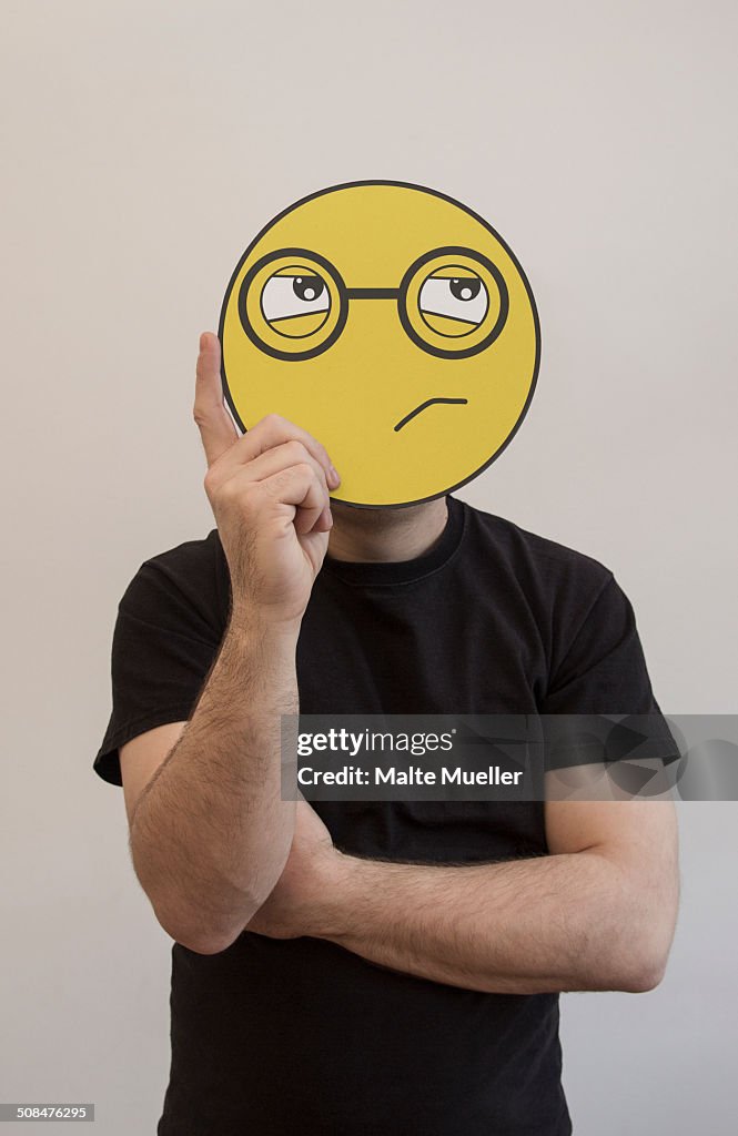 Man holding a confused emoticon face in front of his face