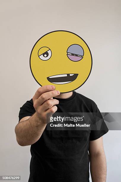 man holding an emoticon face with a black eye in front of his face - black eye stockfoto's en -beelden