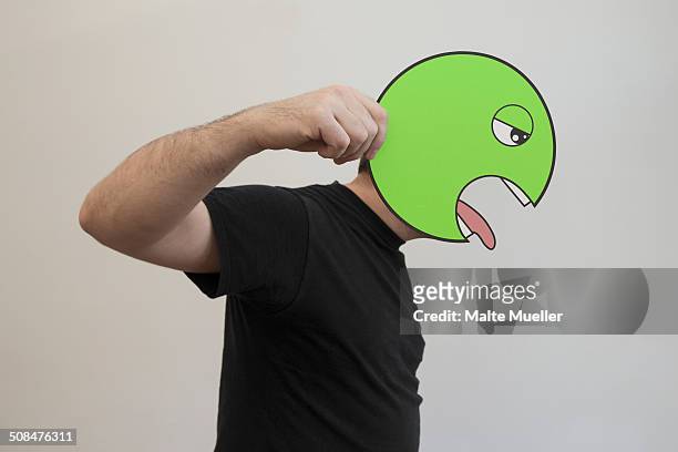 side view of man holding a green vomit emoticon face in front of his face - stick out tongue emoji stock-fotos und bilder
