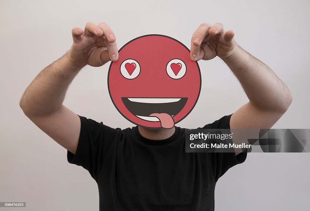 Man holding a romantic emoticon face in front of his face