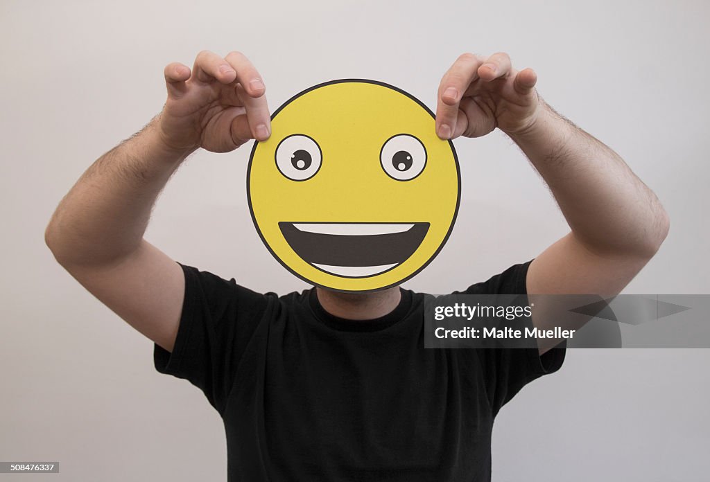 Man holding a really happy emoticon face in front of his face