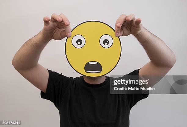 man holding a shocked emoticon face in front of his face - man open mouth stock pictures, royalty-free photos & images