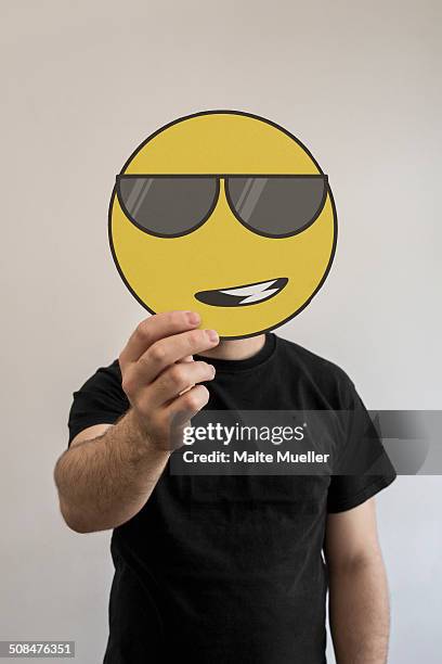 man holding a cool, sunglass wearing emoticon face in front of his face - sunglasses emoji stock pictures, royalty-free photos & images