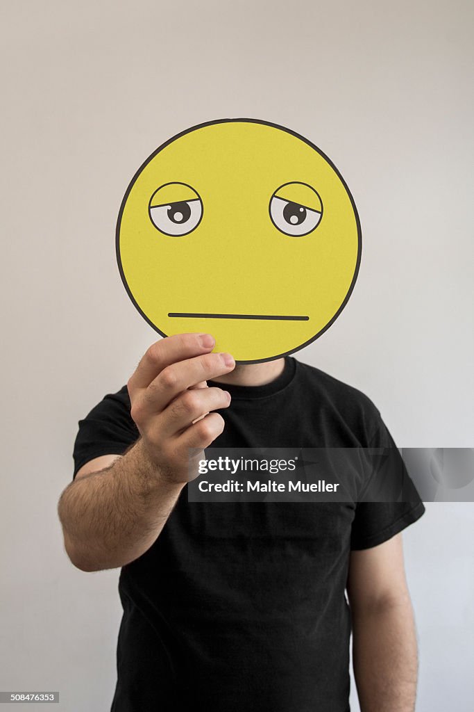 Man holding an exhausted emoticon face in front of his face