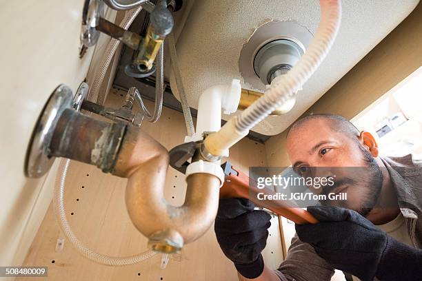 hispanic plumber working under sink - under sink foto e immagini stock