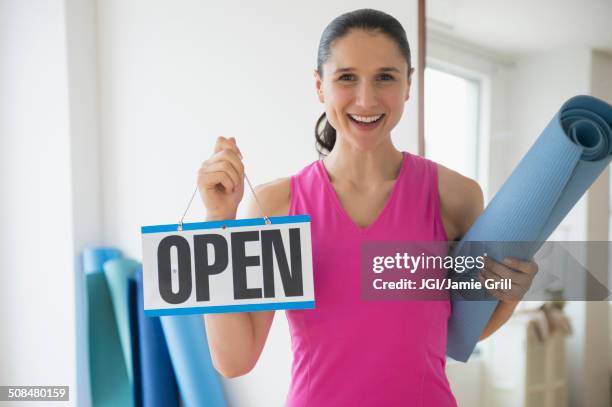 caucasian woman holding open sign in yoga studio - open workouts foto e immagini stock