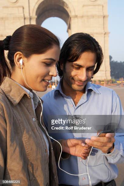 indian couple listening to headphones by monument, delhi, india - india gate photos et images de collection