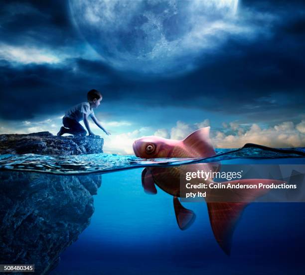 caucasian boy reaching for oversized goldfish in ocean - dream big foto e immagini stock