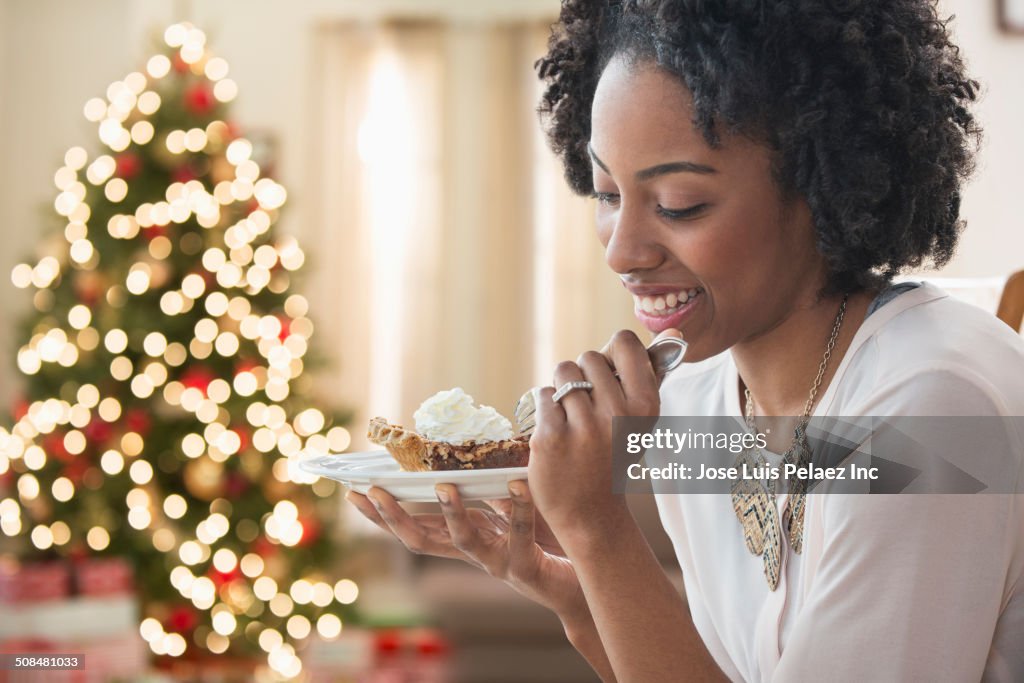 Mixed race woman eating dessert by Christmas tree