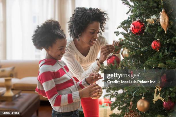 mother and daughter decorating christmas tree - decorare l'albero di natale foto e immagini stock