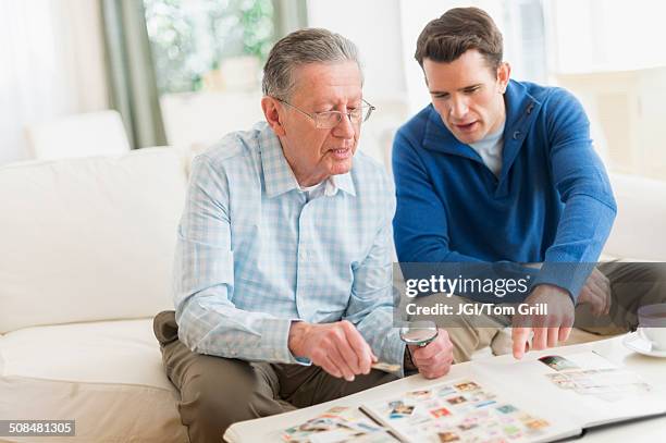 caucasian father and son examining stamp collection - collezionare francobolli foto e immagini stock