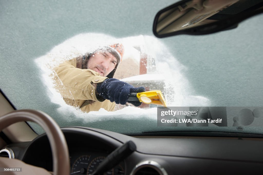 Caucasian man scraping snow off car windshield