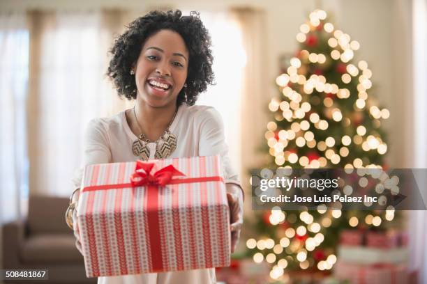 mixed race woman holding christmas gift - giving tree stock pictures, royalty-free photos & images