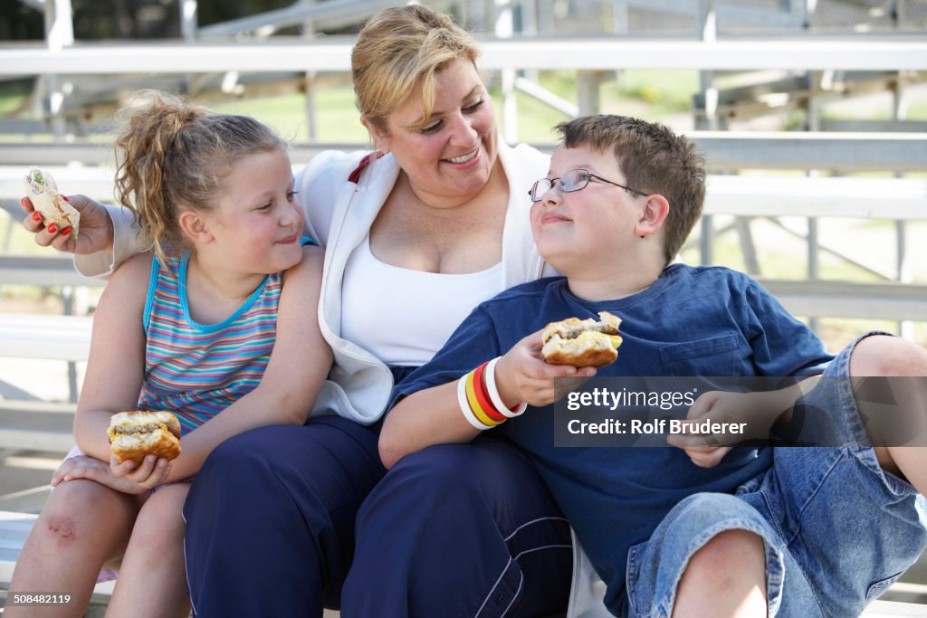 Mother and children eating sandwiches on bleachers