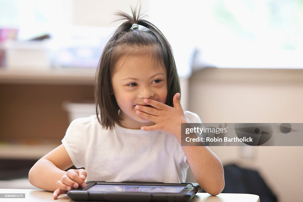 Mixed race Down syndrome student using tablet computer in classroom