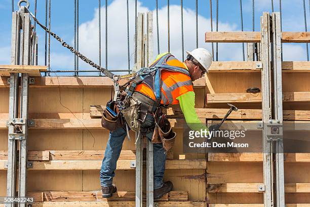 caucasian worker hammering wood at construction site - safety harness stockfoto's en -beelden