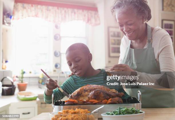older woman and grandson cooking together in kitchen - basted stock pictures, royalty-free photos & images