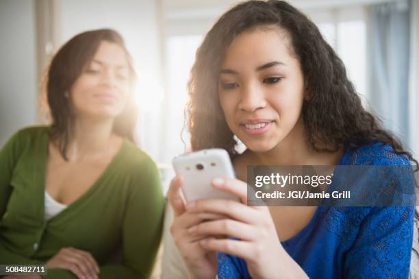 mother watching daughter use cell phone - text messaging mother stock pictures, royalty-free photos & images