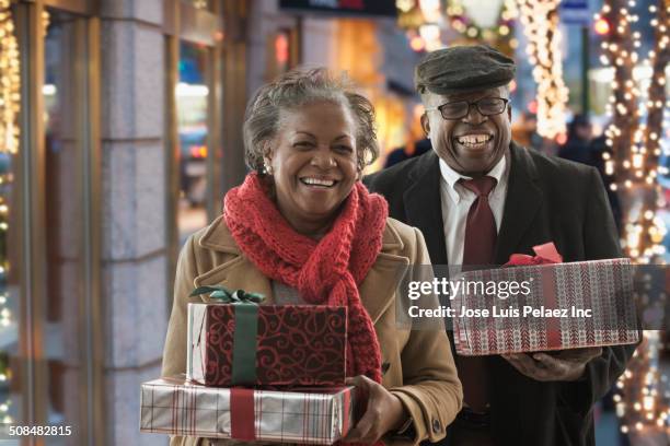 couple carrying christmas gifts on city street - old man woman christmas stock pictures, royalty-free photos & images