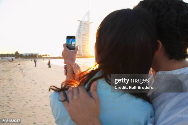 couple taking pictures together on beach, dubai, united arab emirates - dubai strand stock-fotos und bilder