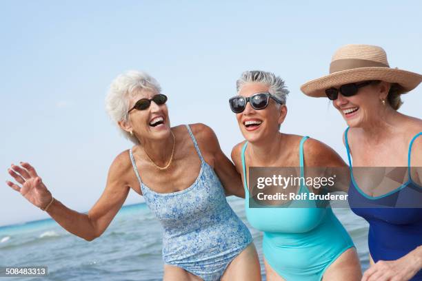 senior women walking on beach - old woman in swimsuit stock-fotos und bilder