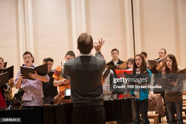 conductor directing choir on stage - coro foto e immagini stock